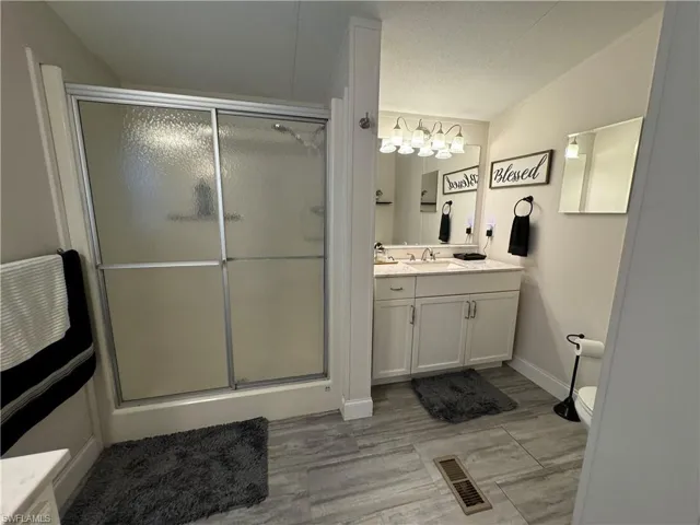 Bathroom featuring hardwood / wood-style floors, vanity with extensive cabinet space, vaulted ceiling, a shower with door, and toilet