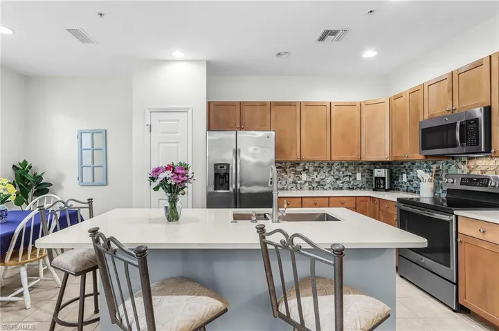 Kitchen with stainless steel appliances, light tile patterned floors, a kitchen island with sink, wood finish cabinets, and decorative backsplash