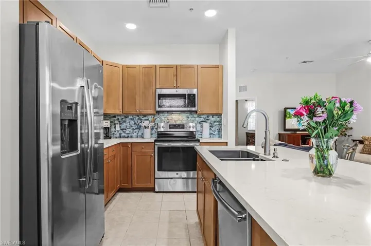 Kitchen featuring stainless steel appliances, light stone countertops, backsplash, wood finish cabinetry, and light tile patterned flooring
