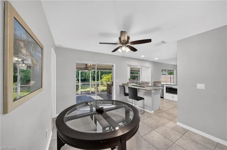 Neutral wall color, ceiling fan with integrated lighting, tiled flooring, kitchen with stone countertops, and sliding glass doors to outdoor area