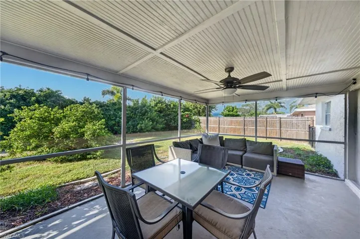 Screened patio featuring a ceiling fan, concrete flooring, and a lush green backdrop