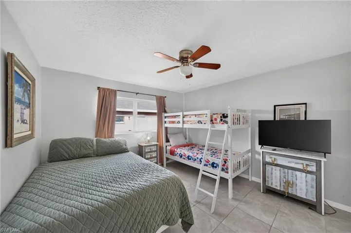 Recessed window with drapes, ceiling fan with light fixture, tiled flooring, and light-toned wall paint