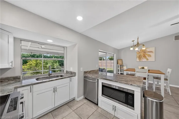 White shaker cabinetry, stainless steel appliances, speckled stone countertops, tile flooring, and recessed lighting
