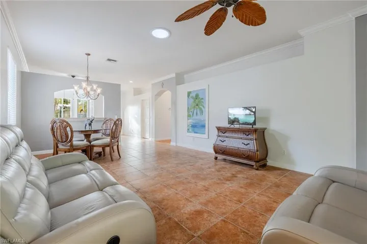 Living room with ornamental molding, light tile floors, and ceiling fan with notable chandelier