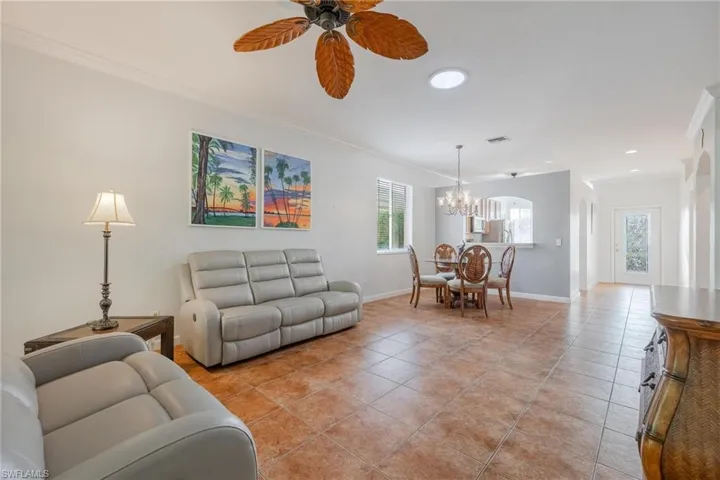 Living room featuring ceiling fan with notable chandelier, light tile floors, and crown molding
