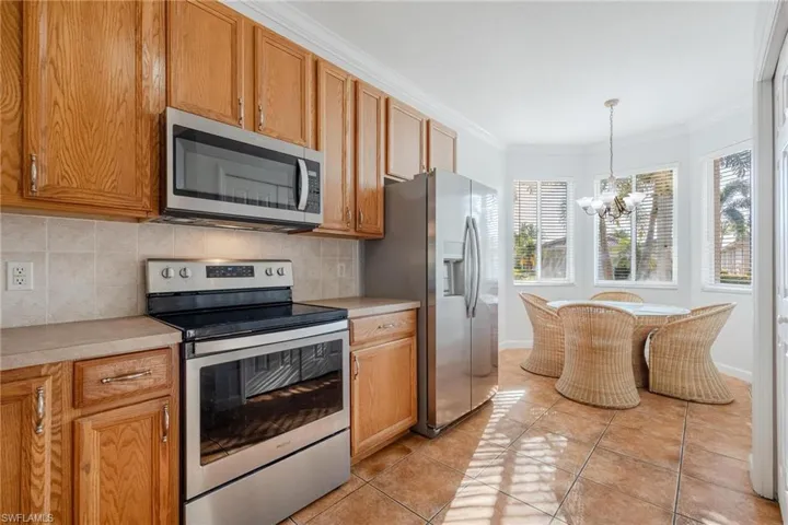 Kitchen with stainless steel appliances, a notable chandelier, hanging light fixtures, backsplash, and light tile floors
