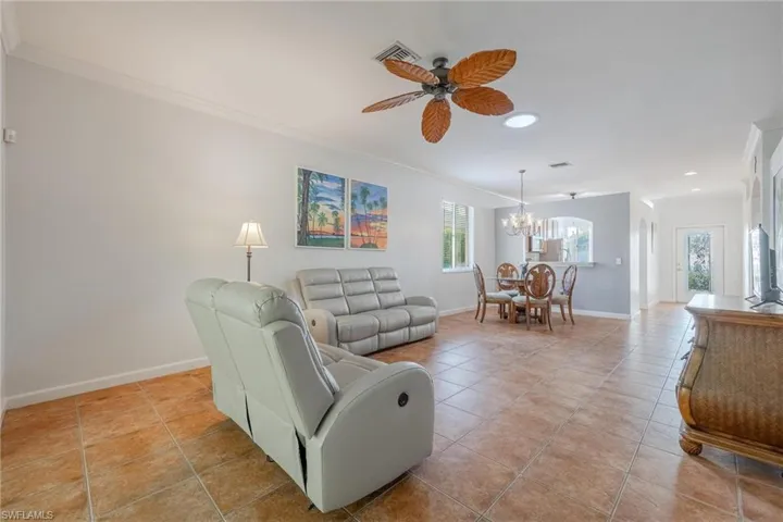 Living room featuring ornamental molding, light tile floors, and ceiling fan with notable chandelier