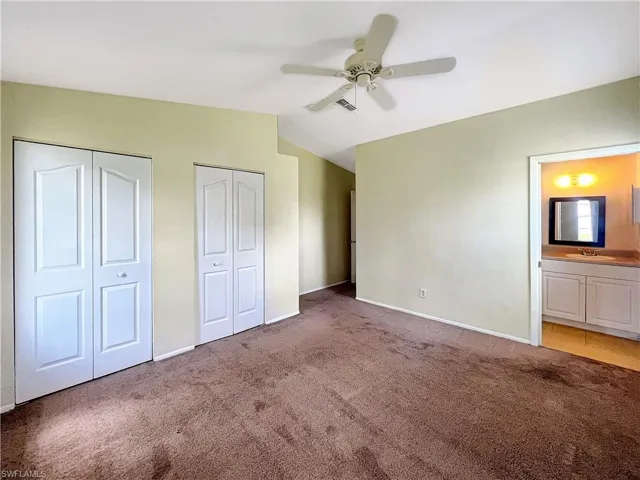 Unfurnished bedroom featuring carpet flooring, multiple closets, ceiling fan, ensuite bath, and lofted ceiling