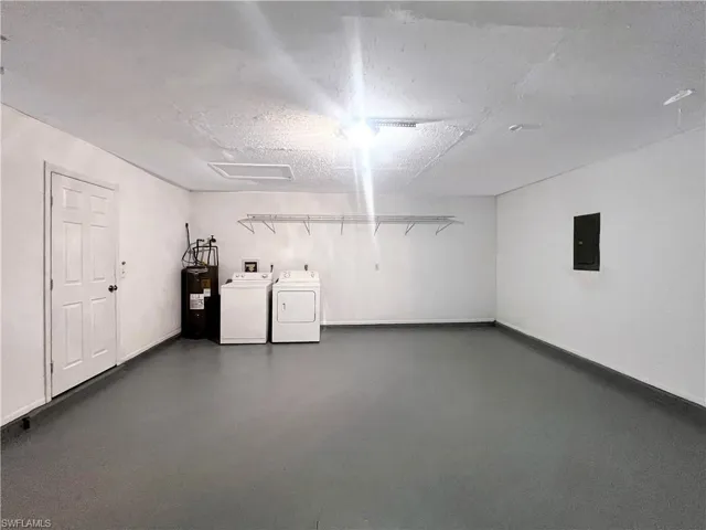 Garage featuring washing machine and clothes dryer, electric panel, and water heater