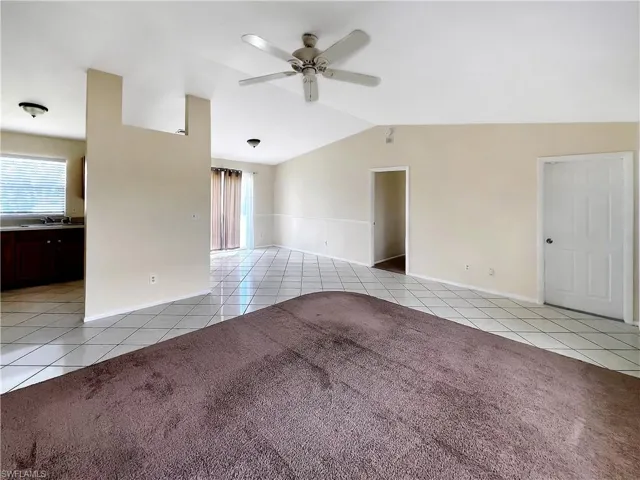 Tiled empty room featuring ceiling fan, sink, and vaulted ceiling