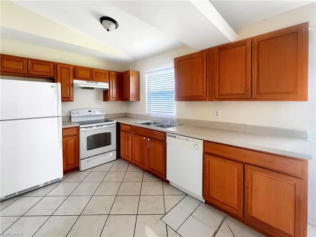 Kitchen featuring lofted ceiling, white appliances, sink, and light tile patterned floors