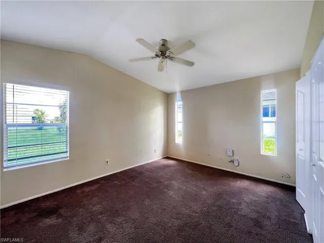 Empty room featuring ceiling fan, dark carpet, and vaulted ceiling