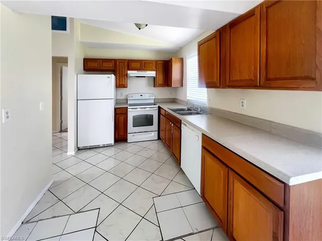Kitchen with light tile patterned floors, white appliances, vaulted ceiling, and sink