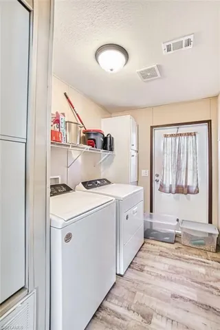 Laundry room with a textured ceiling, light wood finished floors, and independent washer and dryer