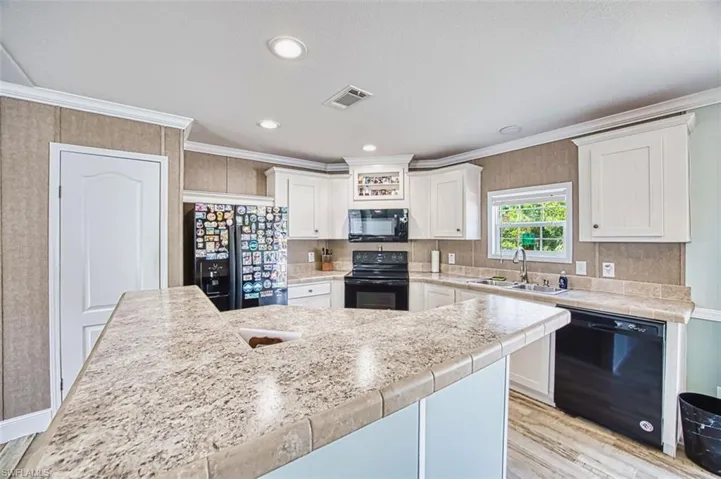 Kitchen featuring light countertops, white cabinets, crown molding, black appliances, and light wood-style flooring
