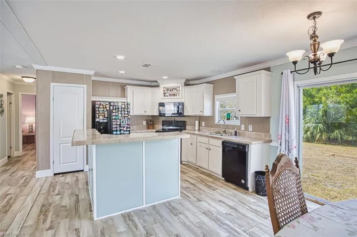 Kitchen with light countertops, white cabinets, crown molding, light wood-type flooring, and hanging lights