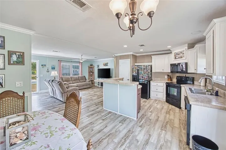 Kitchen with light countertops, black appliances, open floor plan, white cabinets, and ornamental molding
