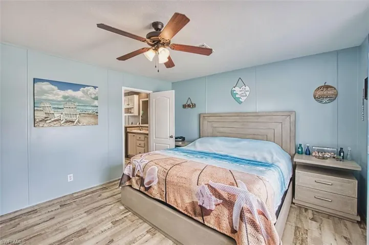 Bedroom featuring a decorative wall, ensuite bath, light wood finished floors, and ceiling fan