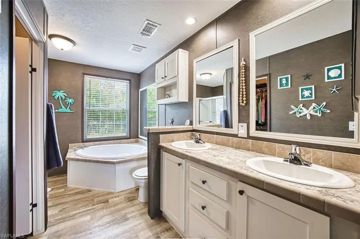 Bathroom featuring double vanity, a textured ceiling, light wood-style flooring, a bath, and a spacious closet