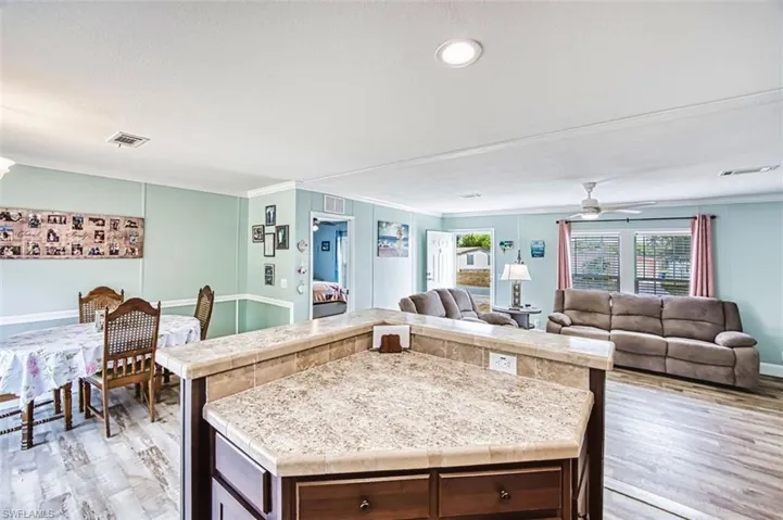Kitchen featuring light wood-type flooring, light countertops, dark wood finish cabinetry, open floor plan, and ornamental molding