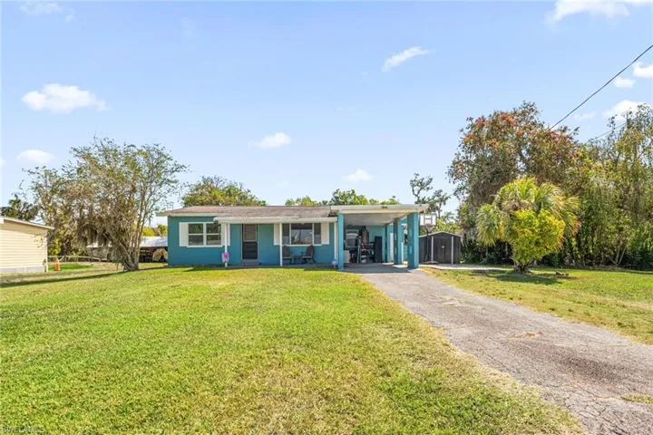 View of front of house with a front lawn, a carport, an outbuilding, and aphalt driveway