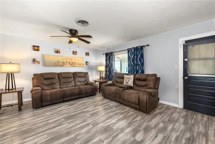 Living room with baseboards, visible vents, wood finished floors, and a ceiling fan