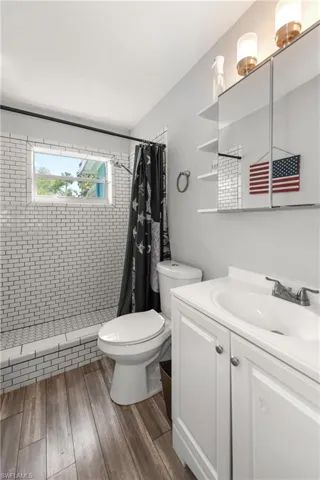 Bathroom featuring vanity, toilet, tiled shower, and wood finished floors