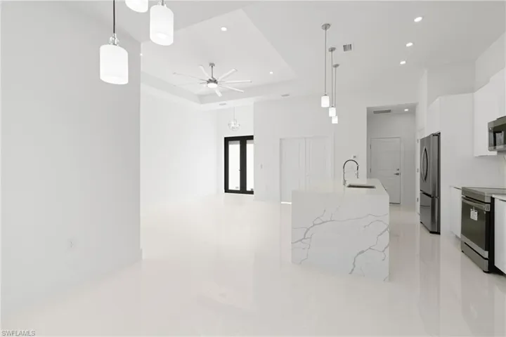 Kitchen featuring decorative light fixtures, a tray ceiling, stainless steel appliances, light stone countertops, and light tile patterned floors