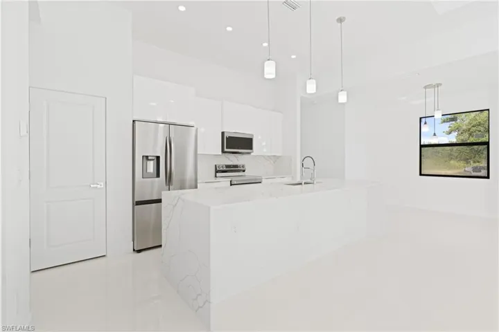 Kitchen with white cabinets, an island with sink, light stone countertops, appliances with stainless steel finishes, and decorative light fixtures