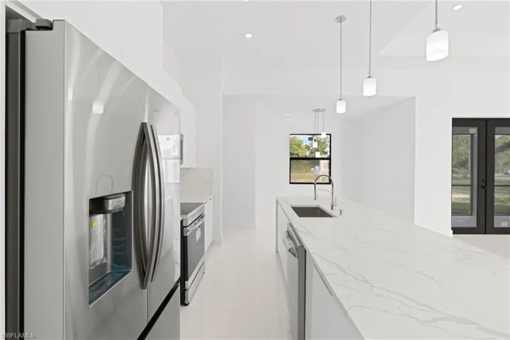 Kitchen featuring decorative light fixtures, sink, light stone countertops, appliances with stainless steel finishes, and light tile patterned floors