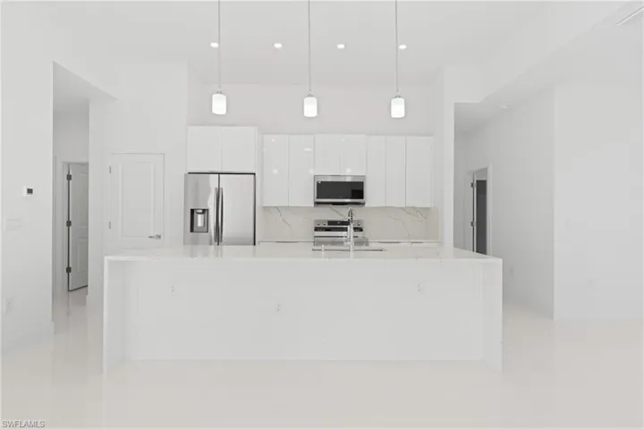 Kitchen featuring decorative backsplash, appliances with stainless steel finishes, pendant lighting, and white cabinets
