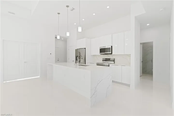 Kitchen featuring appliances with stainless steel finishes, a center island with sink, sink, decorative light fixtures, and white cabinetry