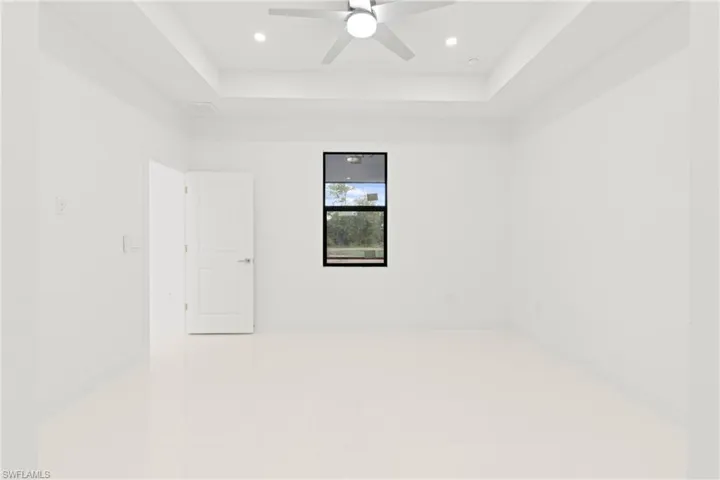 Tiled empty room with ceiling fan and a raised ceiling