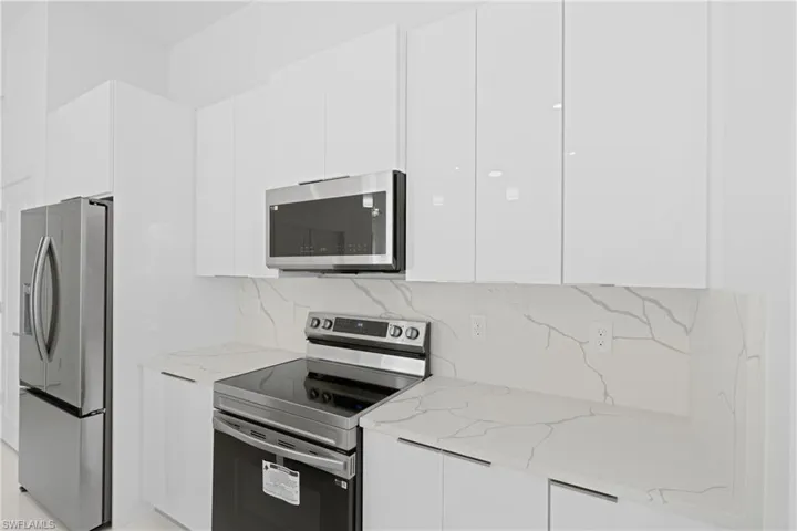 Kitchen featuring white cabinets, tasteful backsplash, light stone countertops, and appliances with stainless steel finishes