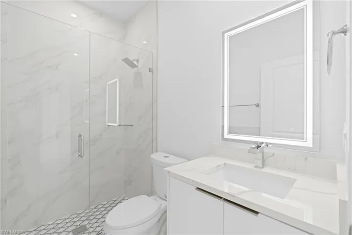 Bathroom with a shower with shower door, vanity, and toilet