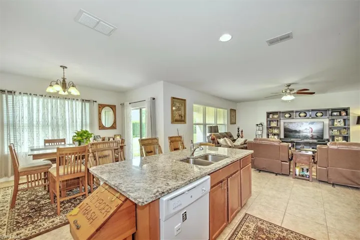 Kitchen with sink, light tile patterned floors, ceiling fan with notable chandelier, an island with sink, and dishwasher