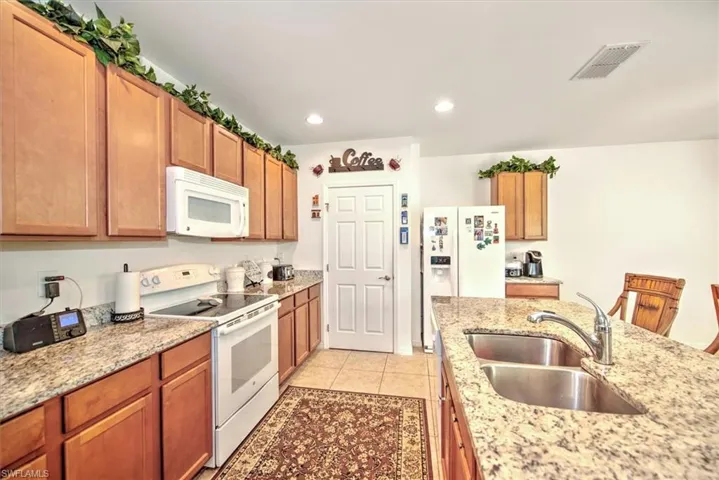 Kitchen featuring light tile patterned flooring, light stone countertops, white appliances, and sink