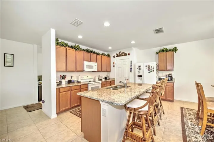 Kitchen featuring white appliances, sink, light stone countertops, an island with sink, and light tile patterned flooring