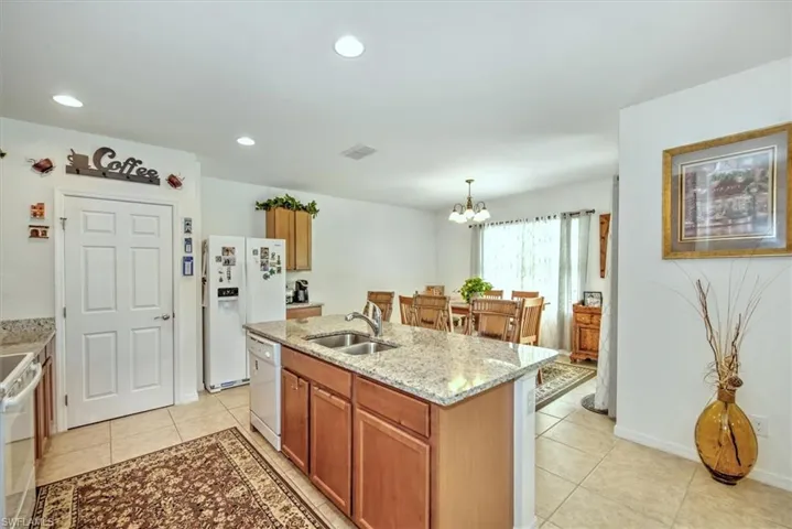 Kitchen with pendant lighting, white appliances, sink, a center island with sink, and light tile patterned floors