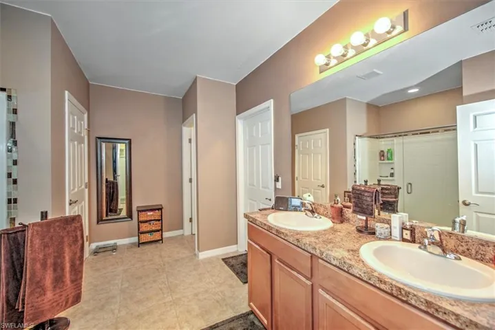 Bathroom with tile patterned floors, a tile shower, and dual bowl vanity