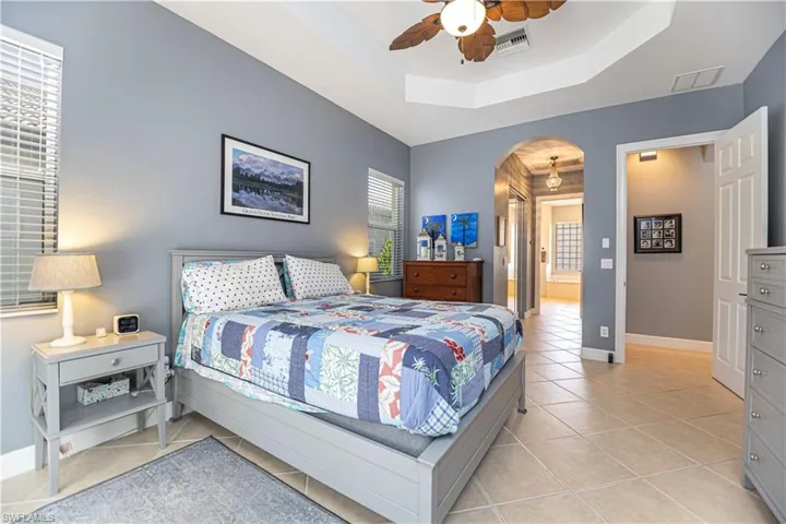 Bedroom with light tile patterned floors, ceiling fan, and a raised ceiling