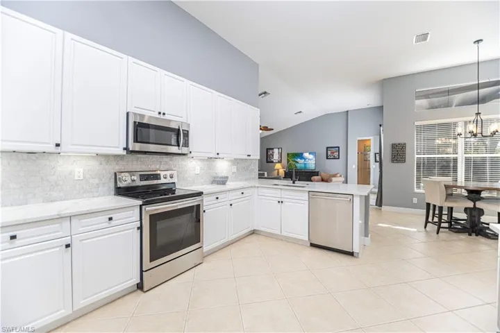 Kitchen featuring stainless steel appliances, white cabinets, lofted ceiling, kitchen peninsula, and backsplash