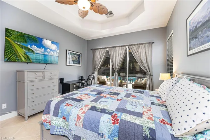 Bedroom with light tile patterned flooring, a tray ceiling, access to exterior, and ceiling fan
