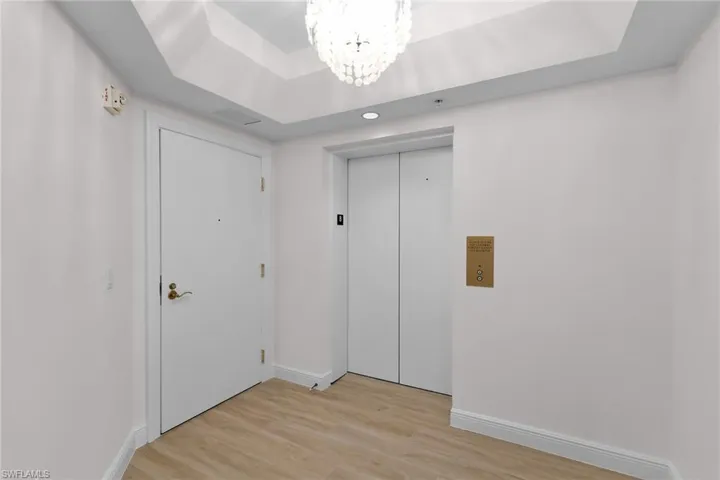 Foyer featuring a chandelier, light wood-type flooring, elevator, and a raised ceiling