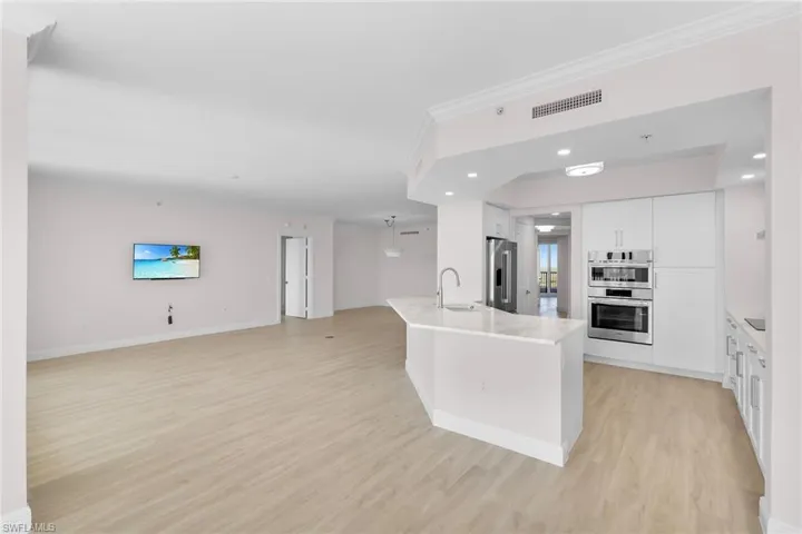 Kitchen featuring white cabinets, open floor plan, light wood finished floors, ornamental molding, and stainless steel appliances