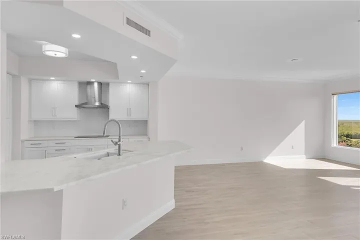 Kitchen with crown molding, light wood-type flooring, light stone counters, recessed lighting, and white cabinets