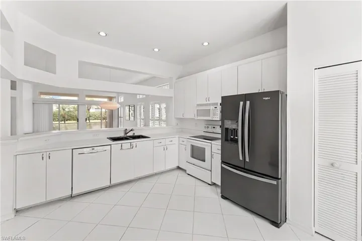 Kitchen featuring white appliances, light countertops, white cabinets, recessed lighting, and light tile patterned floors
