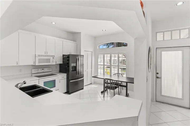 Kitchen featuring white appliances, light countertops, white cabinets, recessed lighting, and light tile patterned floors