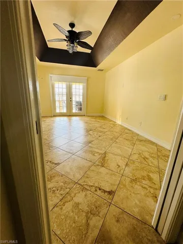 Tiled spare room featuring ceiling fan, a raised ceiling, and french doors