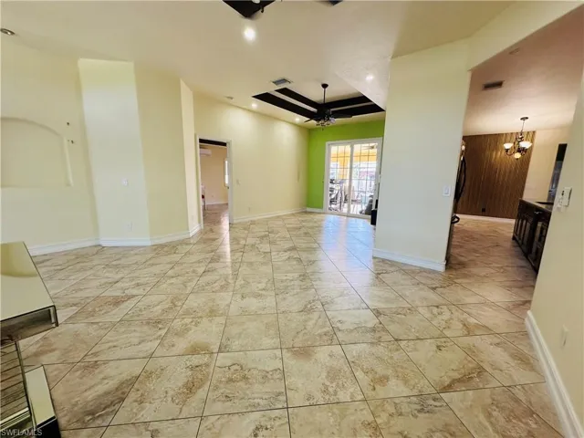 Empty room with ceiling fan with notable chandelier, light tile patterned flooring, and a tray ceiling